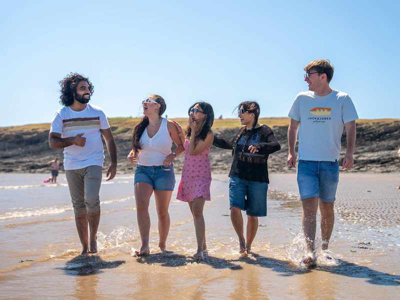 A group of people walking along the sandy beach, enjoying the sun and ocean waves in the background.