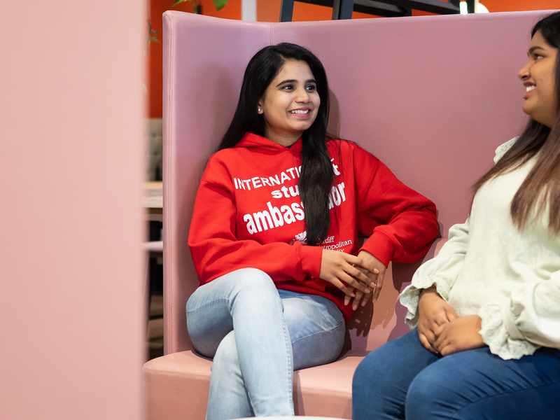 Two women engaged in conversation while seated on a pink couch, creating a warm and inviting atmosphere.