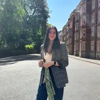 A woman wearing a plaid jacket and jeans stands confidently in the middle of a street.