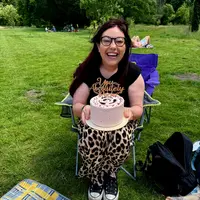 A woman sitting in a lawn chair, smiling while holding a decorated cake in her hands.