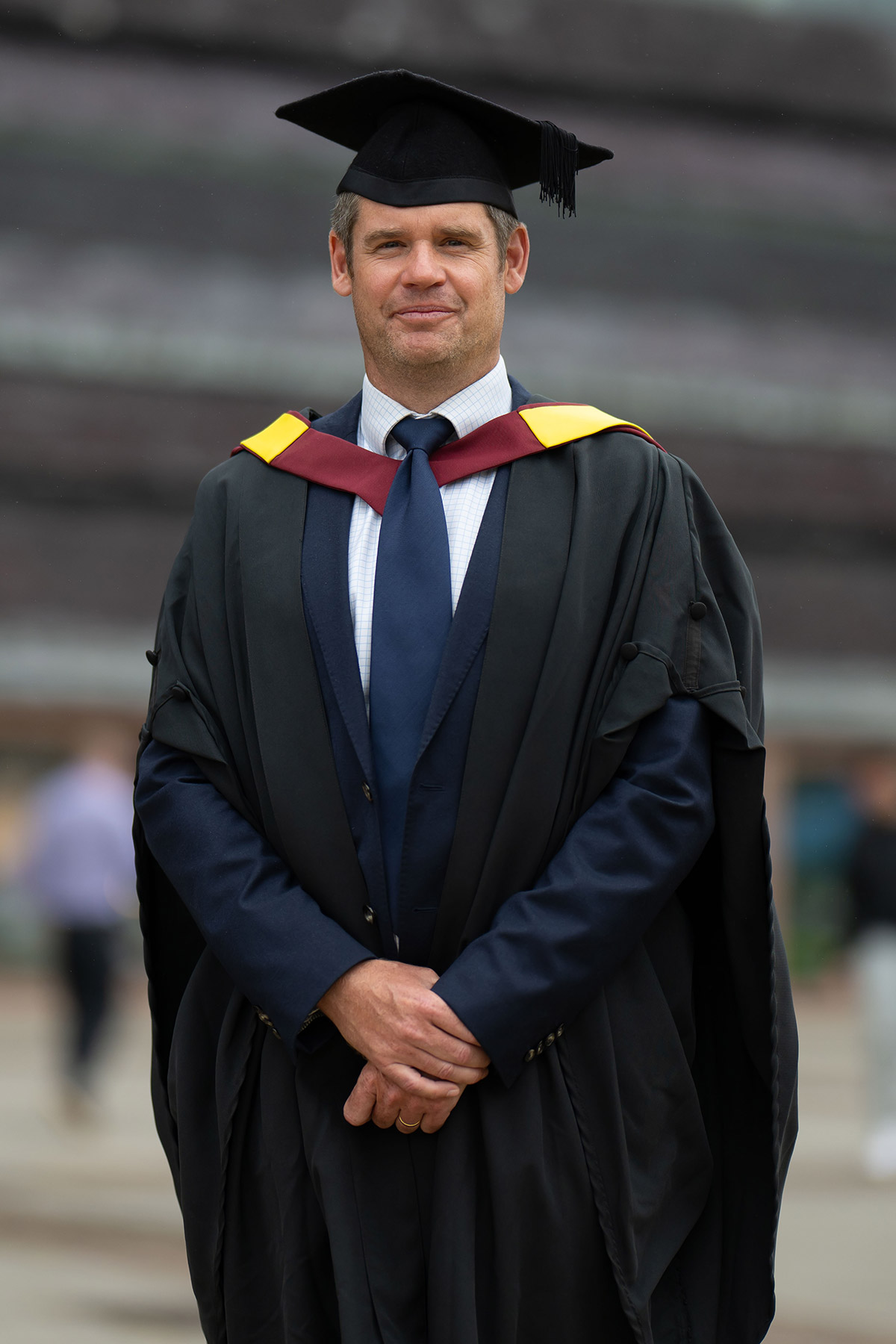 A man wearing a graduation gown and tie, smiling proudly at his graduation ceremony.