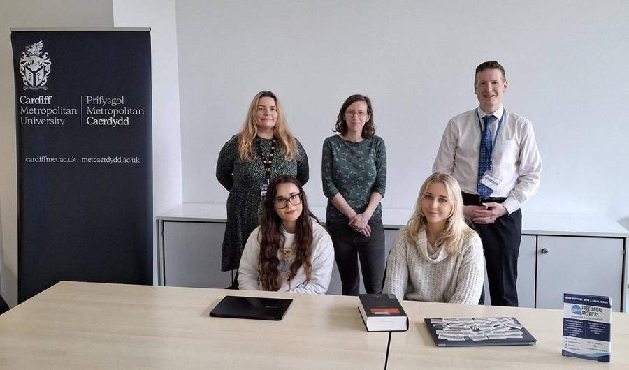 Five people gathered around a table. On the table are two laptop computers and a hardback book.