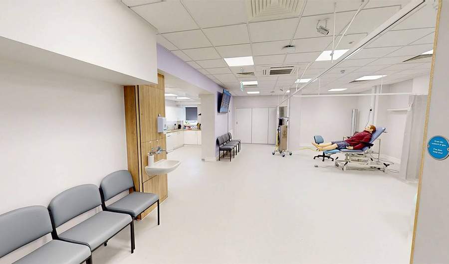 A large white room. In the background, a simulated patient lies on a trolley.