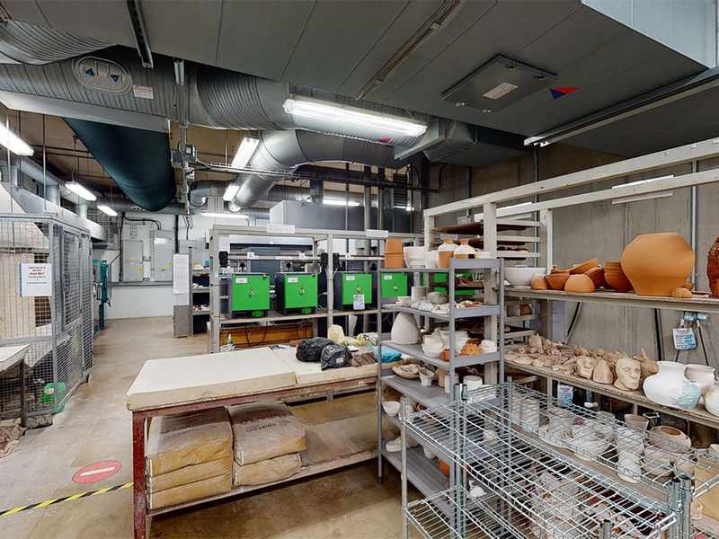 Shelves of completed ceramics in front of work tables and supply shelves