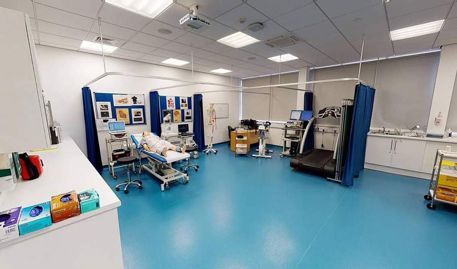 A large room with a height-adjustable bed, treadmill, and medical diagnostic equipment.