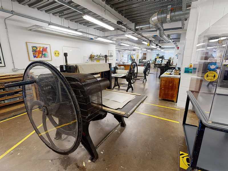 Printing press as the focus of a wide shot of the Printmaking Workshop