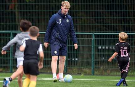 A football coach controls a football during a game of football with young children
