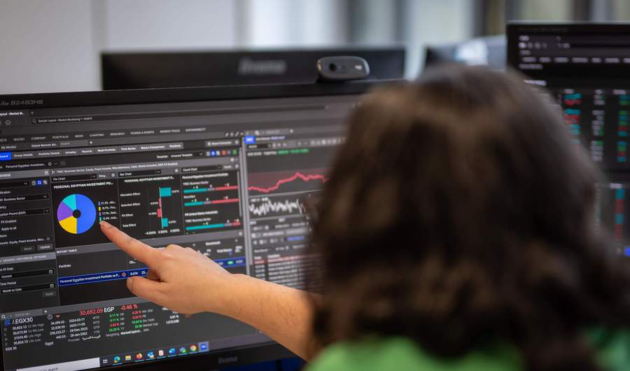 A person points to a large computer monitor showing financial charts.