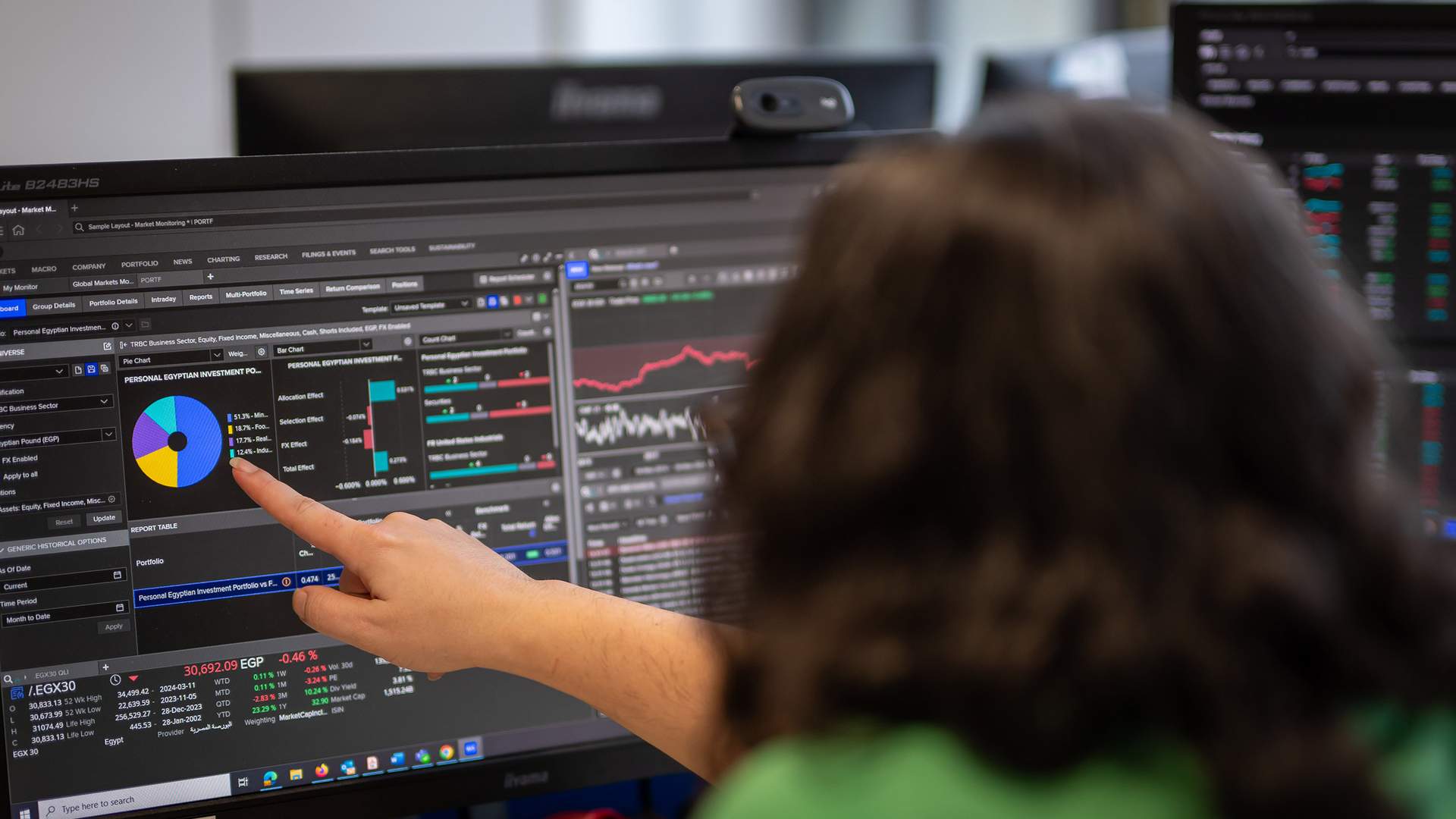 Two men are standing in a modern building with large windows. One is leaning against a wooden railing, wearing a red shirt and cap, while the other stands facing him, wearing a white shirt and watch. They are smiling and engaged in conversation.