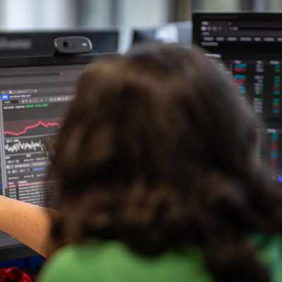 A person in a yellow jacket smiles in front of a modern building with the Cardiff Metropolitan University sign. The sky is overcast, and the building has illuminated lights.