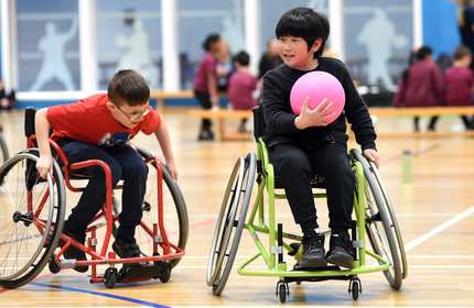 Two young children in wheelchair play a game involving a pink ball