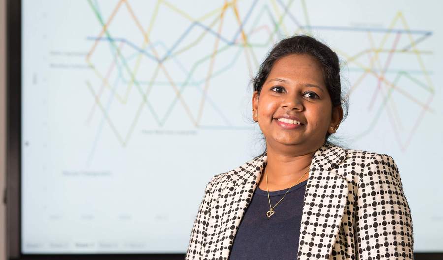 A person stands in front of a large screen showing line charts.