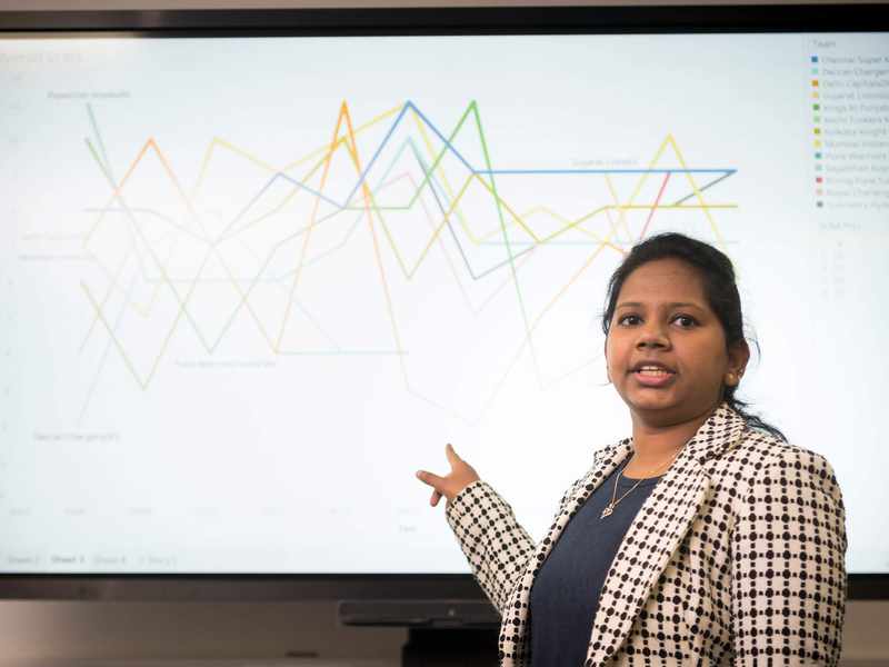 A person points to line charts on a large screen.