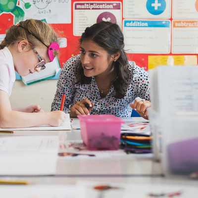 A woman sits on the floor with a young child who is playing on a unicorn ride-on toy. The room is decorated with colorful toys, wall stickers of trees and animals, and foam play mats. The atmosphere is playful and engaging.