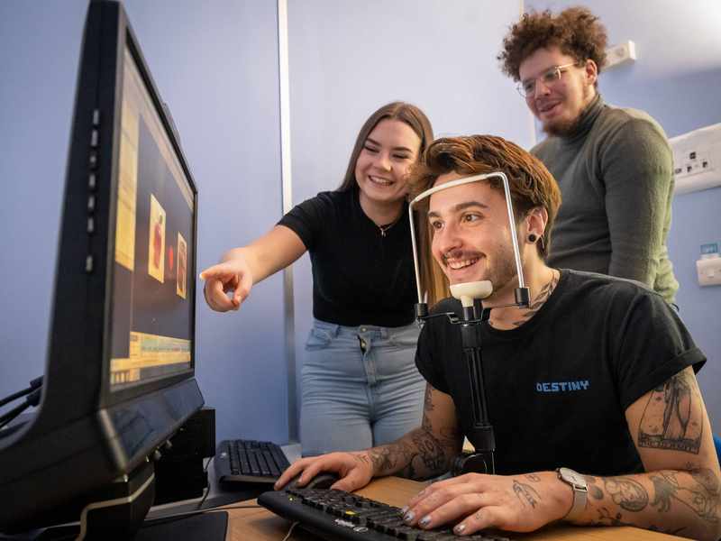 A person sits facing a computer screen. Their chin is resting on a stand.