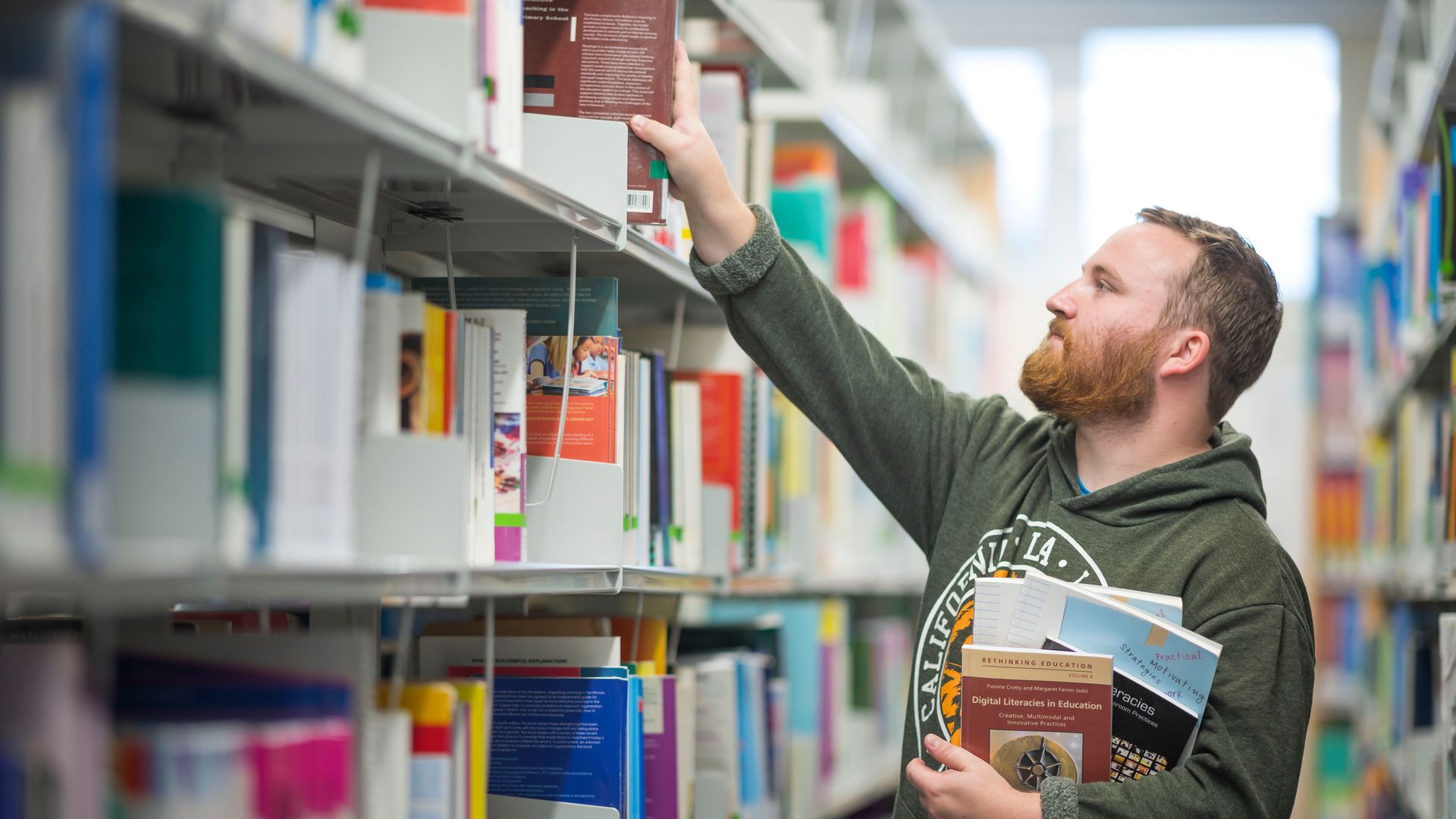 Student reaches up for a book to add to the collection in his other hand