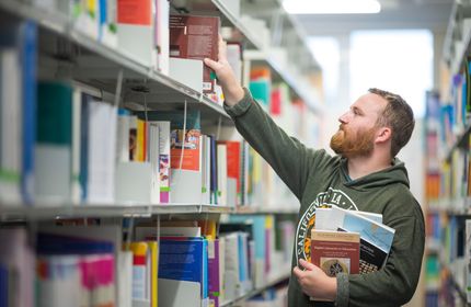 Student reaches up for a book to add to the collection in his other hand