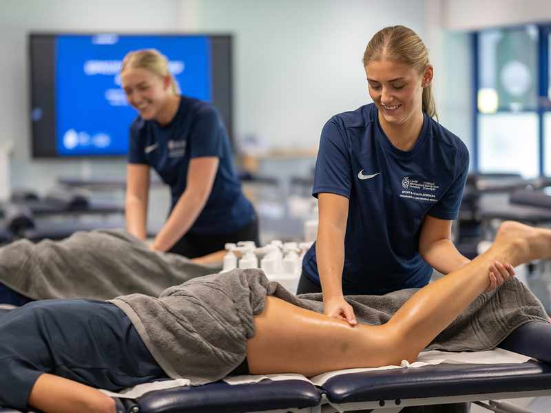 Two sports therapy students practice massage techniques on a patient in a training environment.
