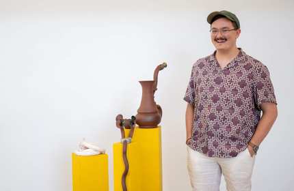 A person stands next to a display of three ceramic objects, each mounted on a tall pedestal.