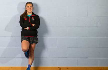 Naomi Davies stands leaning against a grey wall