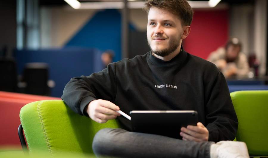 A person sits on a couch with a tablet computer resting on their knee.