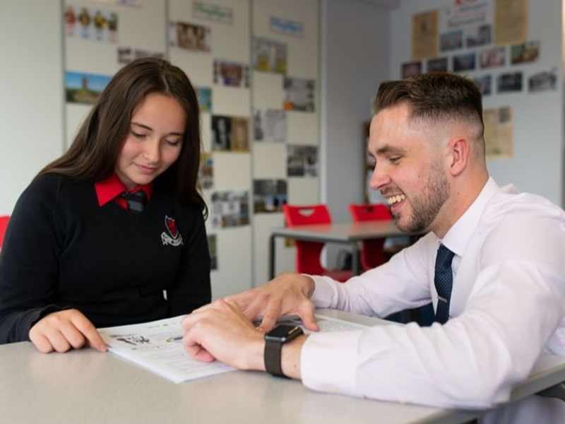 Sion Davies leans down on a table to help a pupil with their work