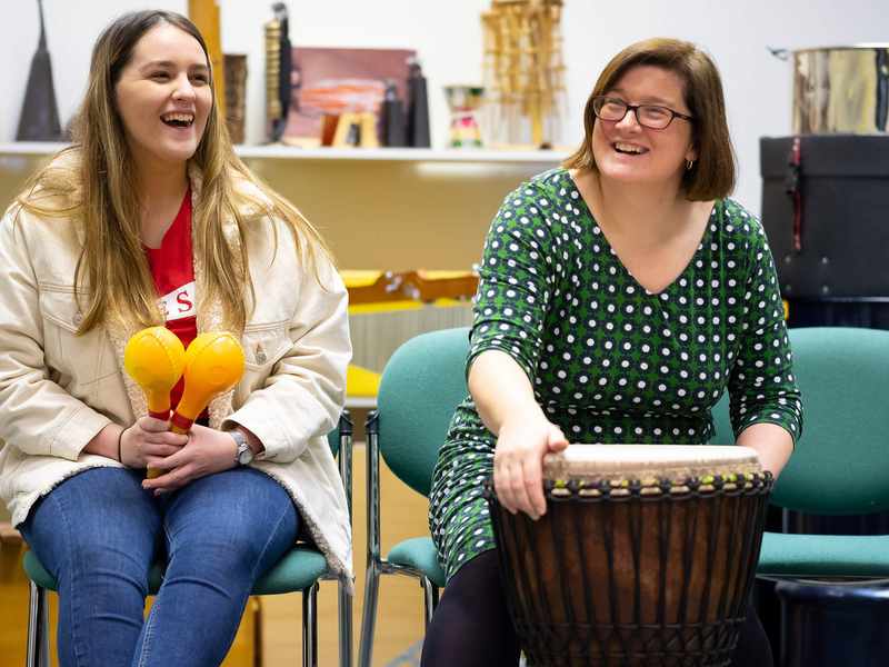 Two people sit in chairs, each holding a percussion musical instrument.