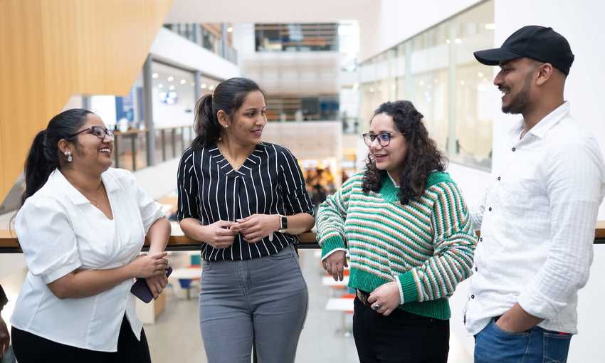 Four people talking to each other on a balcony in an atrium space.