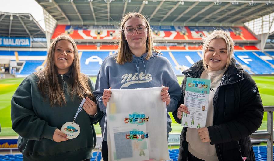 Three young women in the stands of a sports stadium hold Quick Change branded merchandise