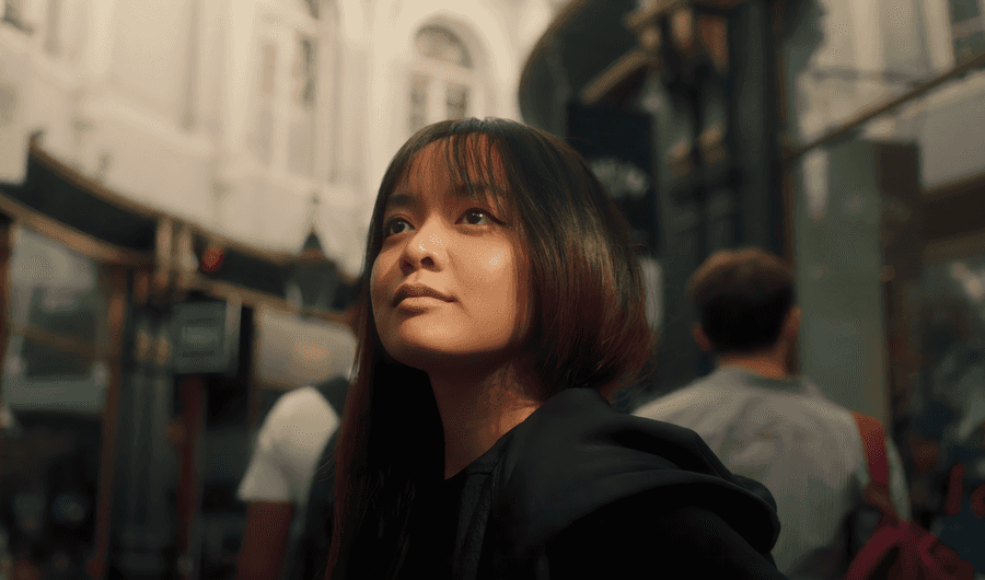 A woman gazes upward at the sky while strolling along a city street, embodying a moment of reflection and wonder.