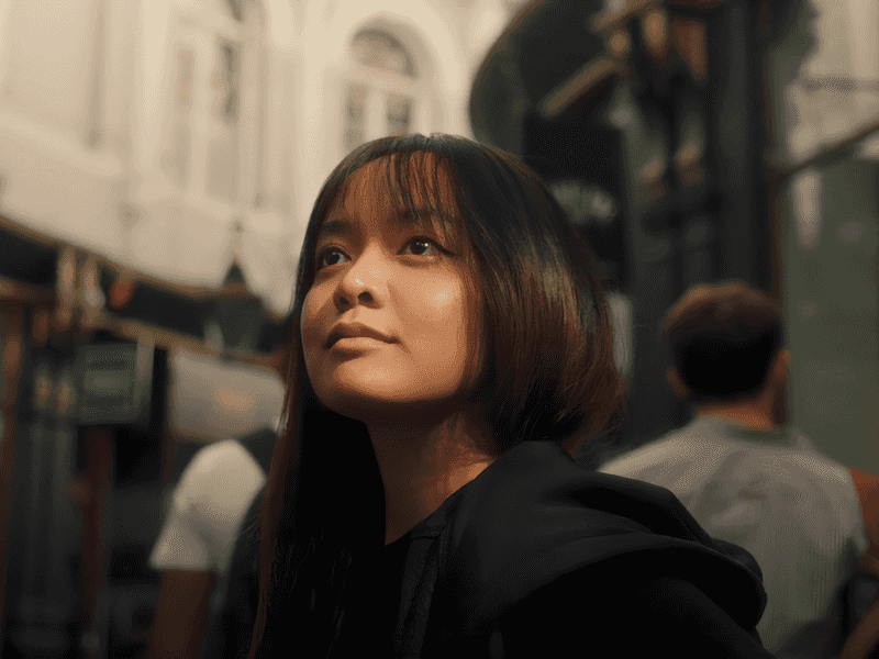 A woman gazes upward at the sky while strolling along a city street, embodying a moment of reflection and wonder.