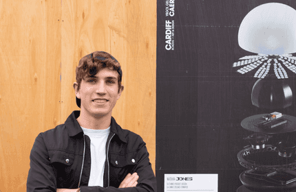 A young man stands beside a poster featuring a stylish lamp design.