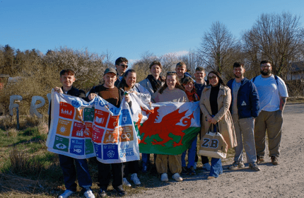 A group of young adults pose for a photograph holding up a flag and banner