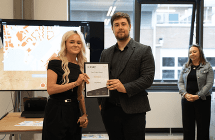 A woman in a dress receives an award from a man in a black dress