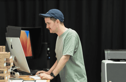 A man wearing a hat is focused on working at his computer.